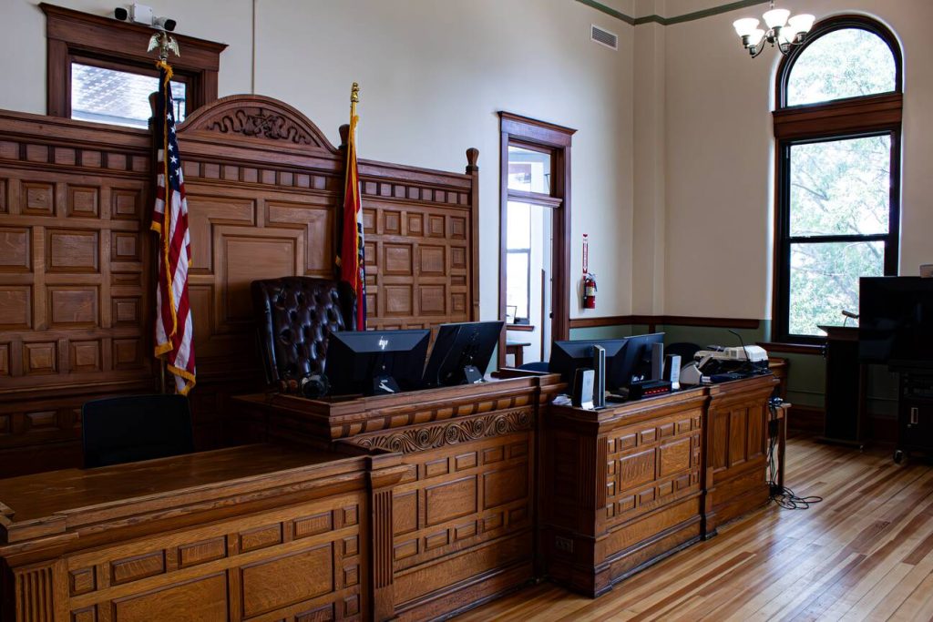 An empty courtroom with judge's bench and American flags representing justice system environment where one aims to win a court case.