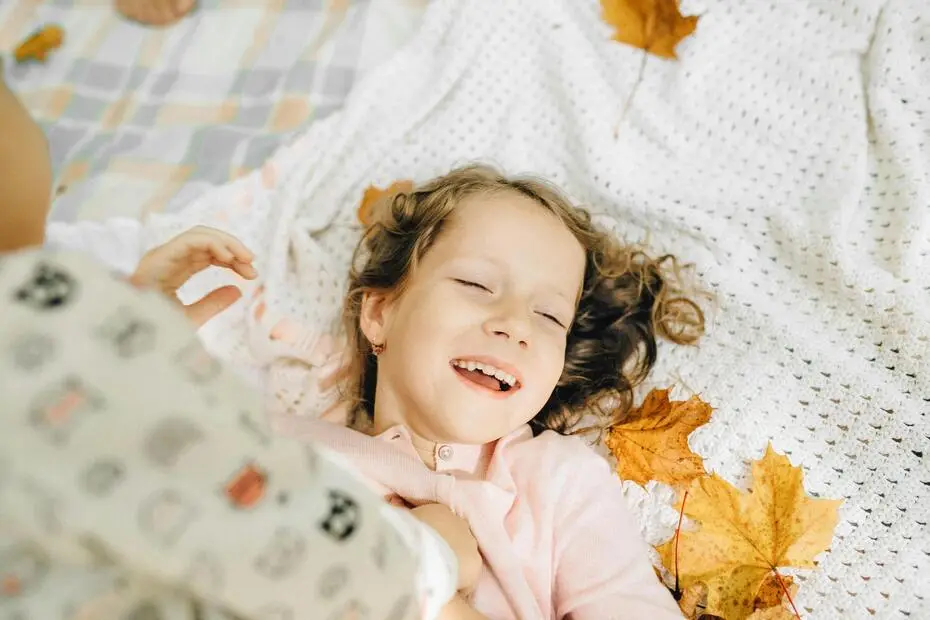 Child lying on a White Fabric with yellow flowers around laughing with a eyes closed
