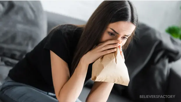 Woman in distress using a paper bag to control breathing, showing signs of an anxiety or panic attack.