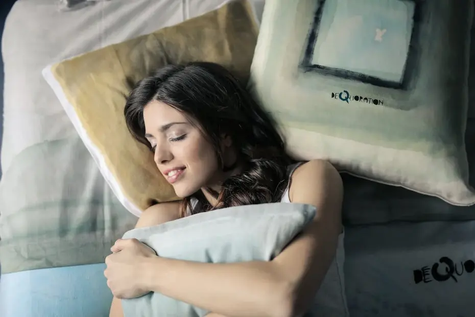 Woman sleeping peacefully on a gray and white bedspread, hugging a pillow for comfort and smiling in her dream.