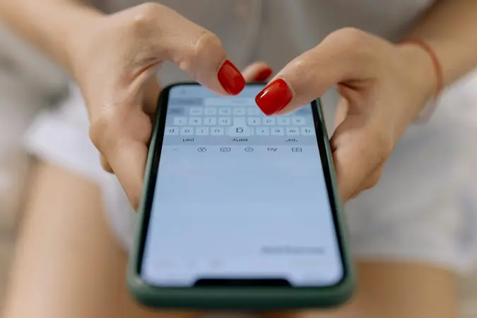 Close-up of hands typing on a smartphone with red nail polish