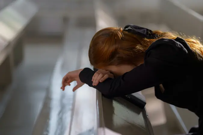 A woman with reddish hair praying in a church pew, resting her head on her arms, with a Bible nearby in a calm, reflective setting