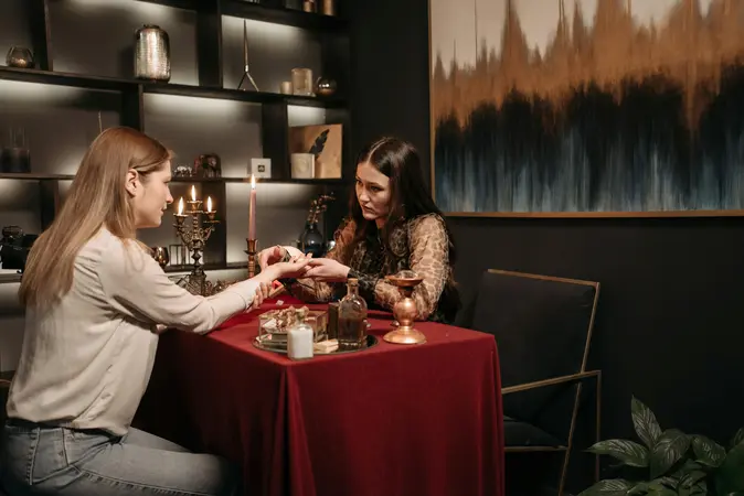 A woman having her palm read by a fortune teller across a candle-lit table, representing beliefs in psychic surveillance and mind reading tactics.
