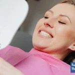 A young woman with a bright smile examining her teeth after braces treatment and whitening at the dental clinic